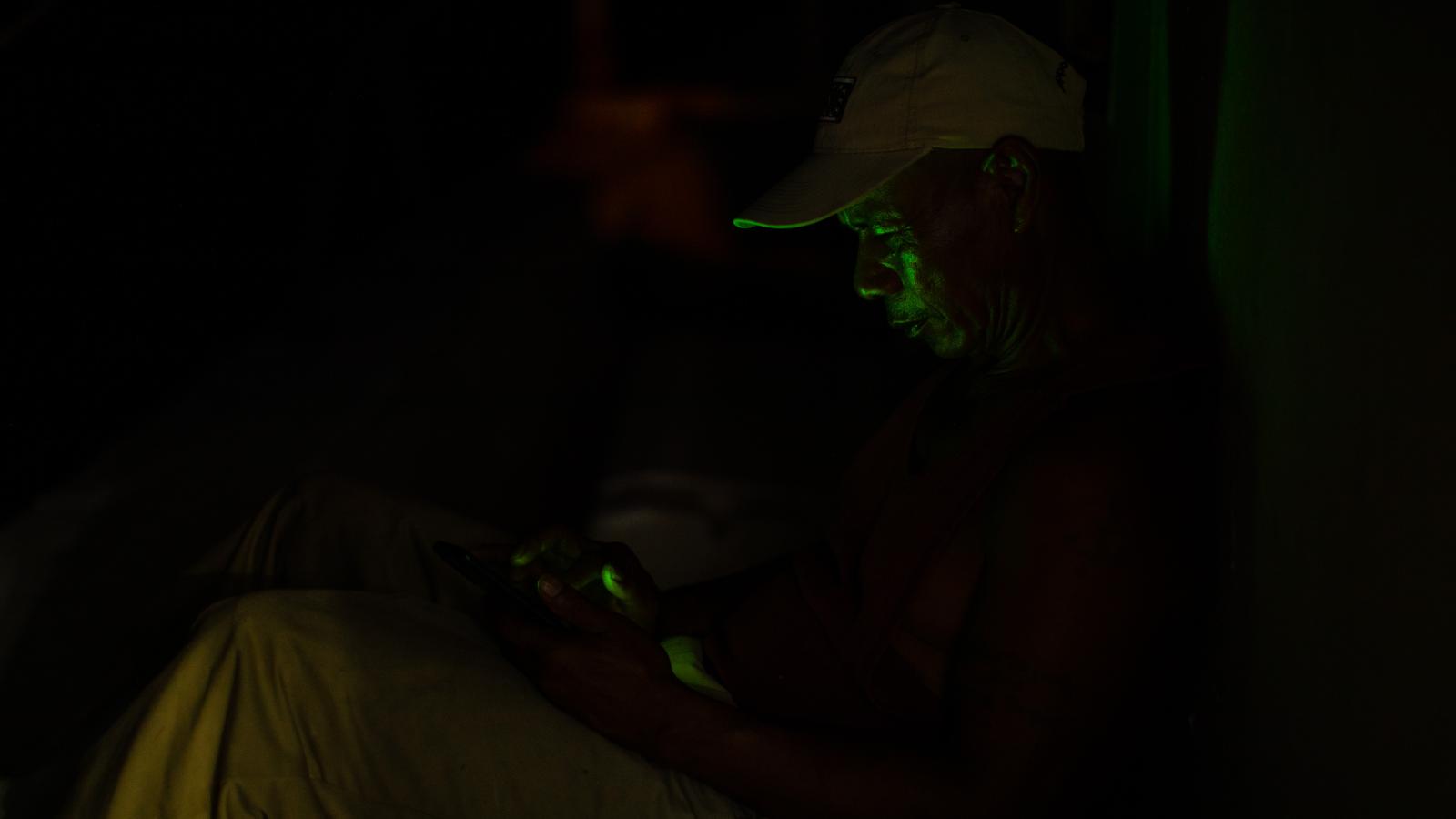 A deck hand dimly lit by the light of his phone.