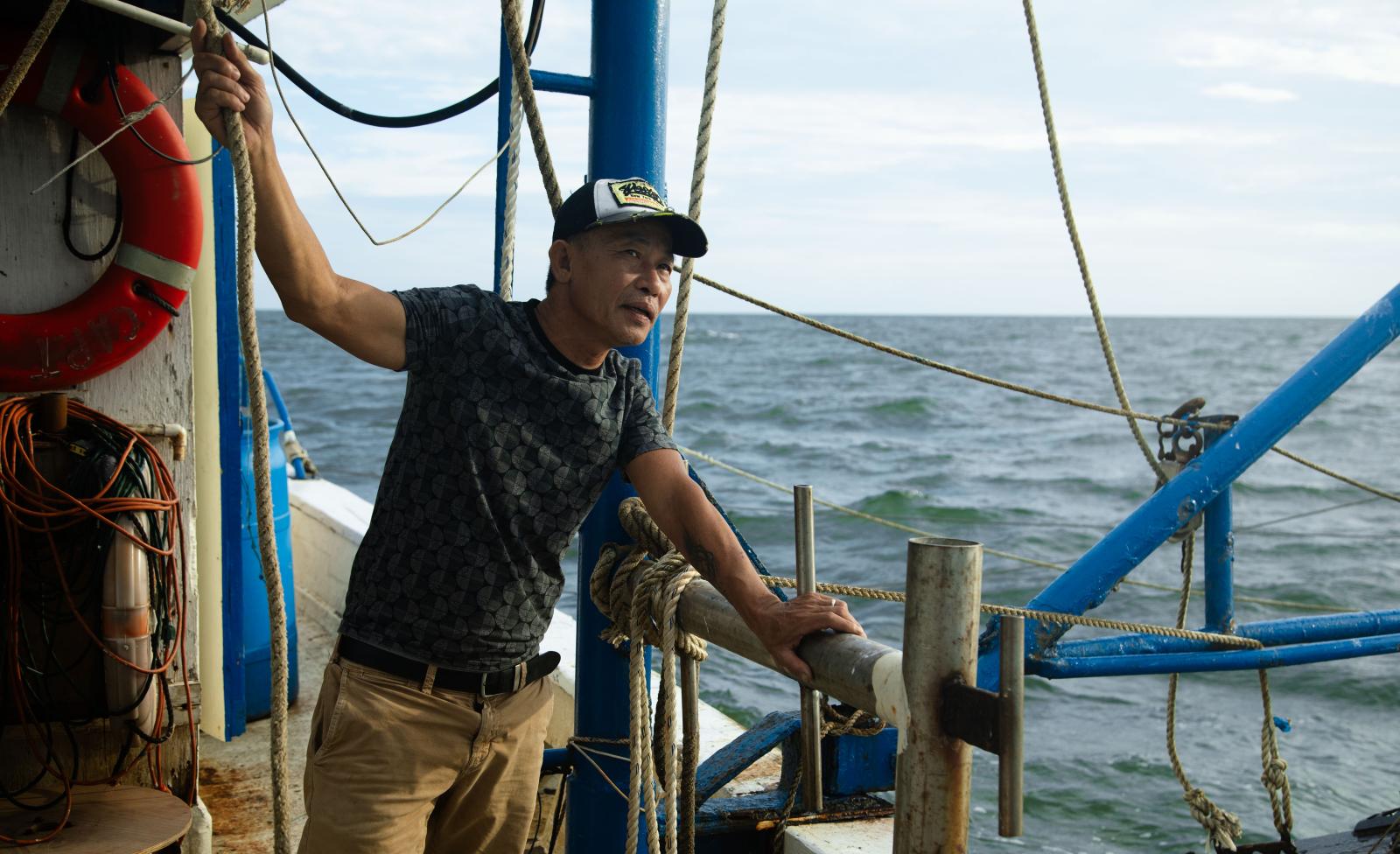A deck hand holds a rope while traveling on the boat.